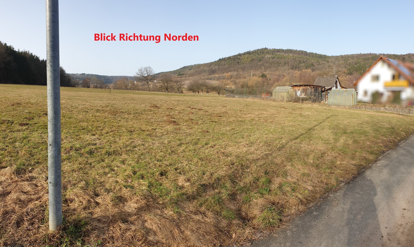 Open field with edge path, post on the left, hill in the background, red text indicating view to the north.