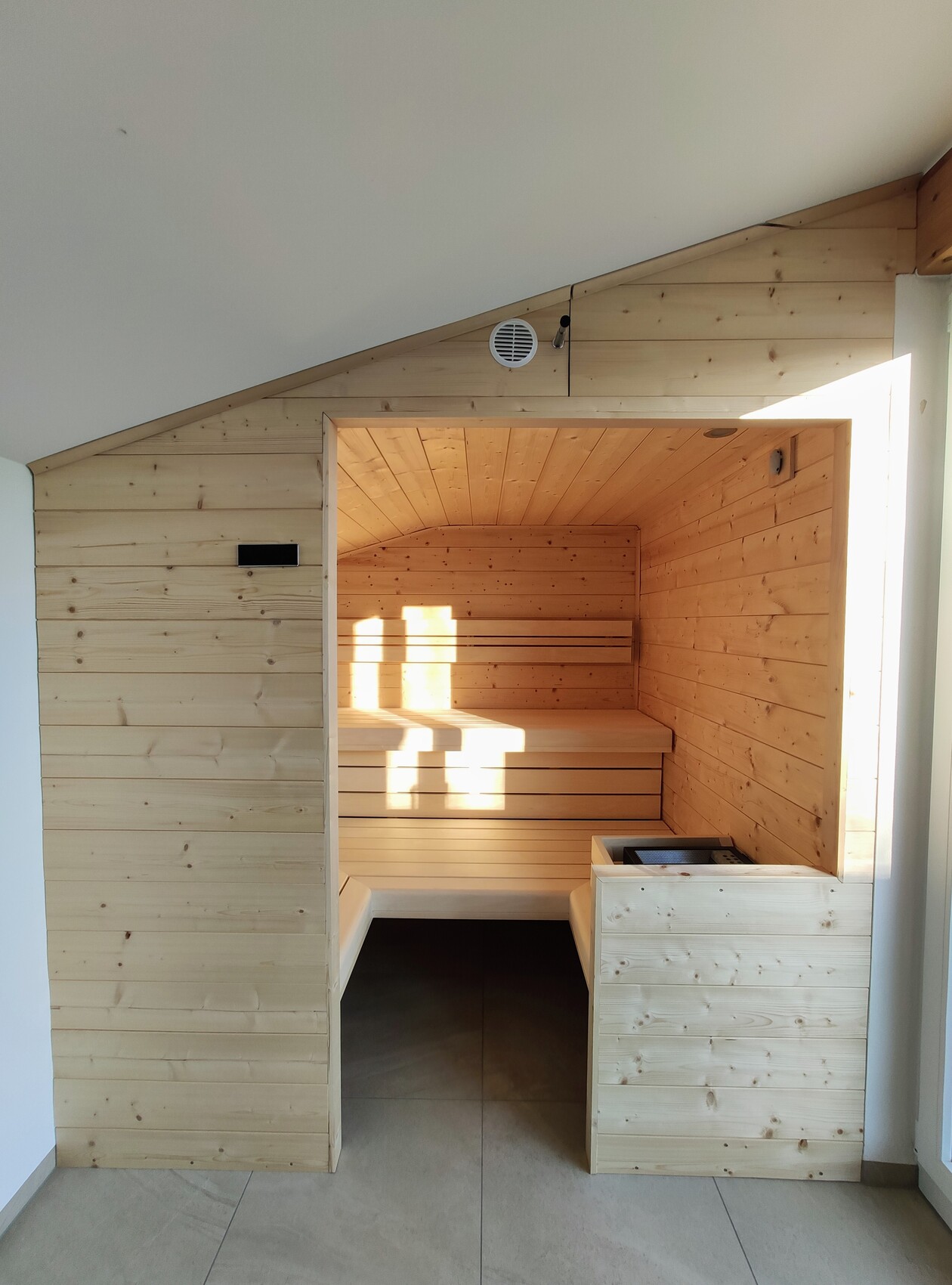 Wood sauna with interior bench, light wood paneling, stove on the right, warm light inside