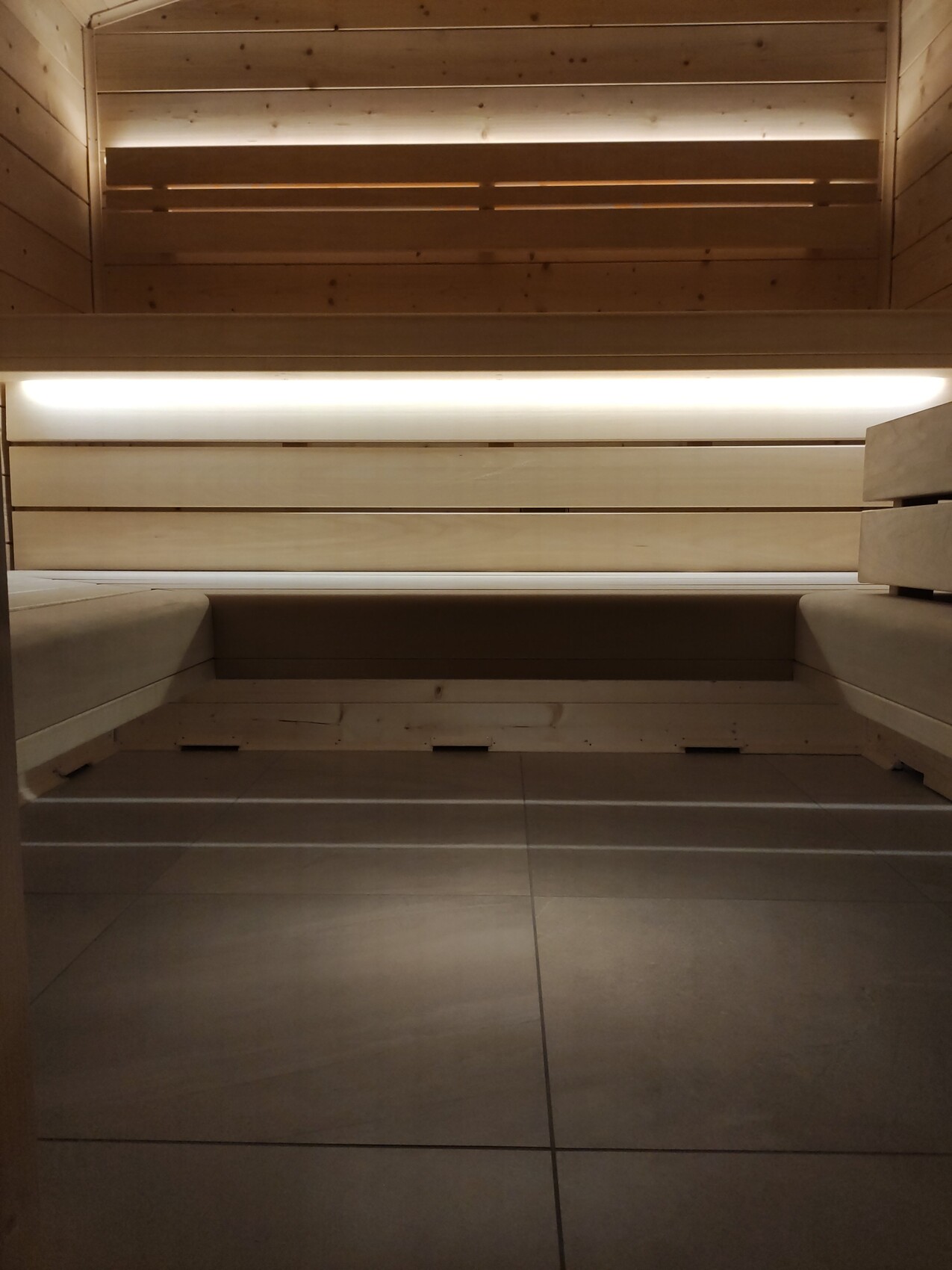 Sauna interior with wooden benches, warm lighting, wood walls, and tiled floor.