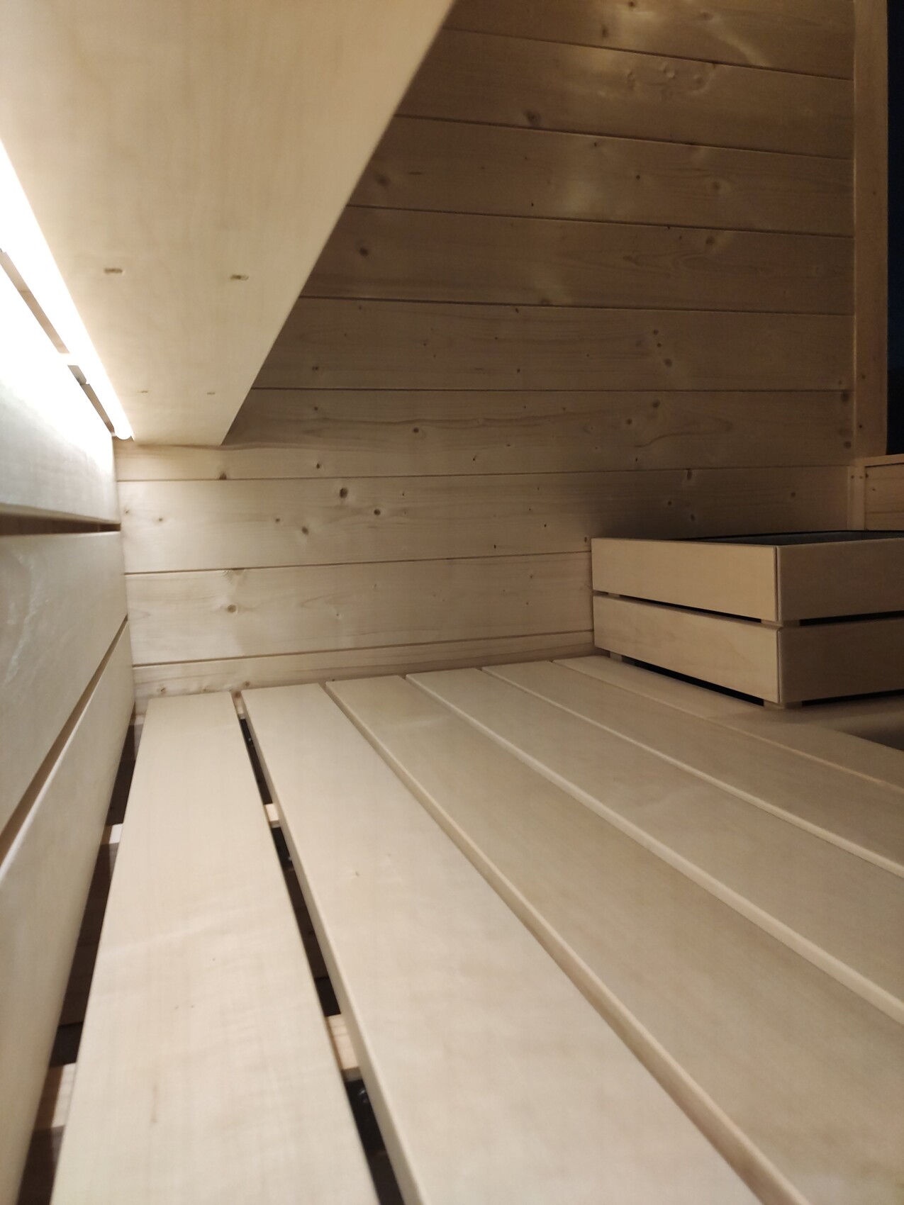 Wood sauna interior with multiple bench levels, wood walls, and warm lighting.