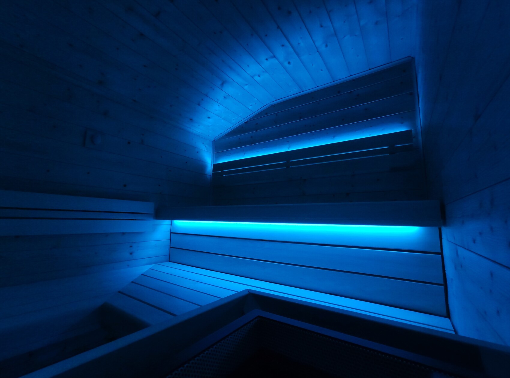 Modern sauna interior with wood paneling, blue LED lighting, and multiple benches