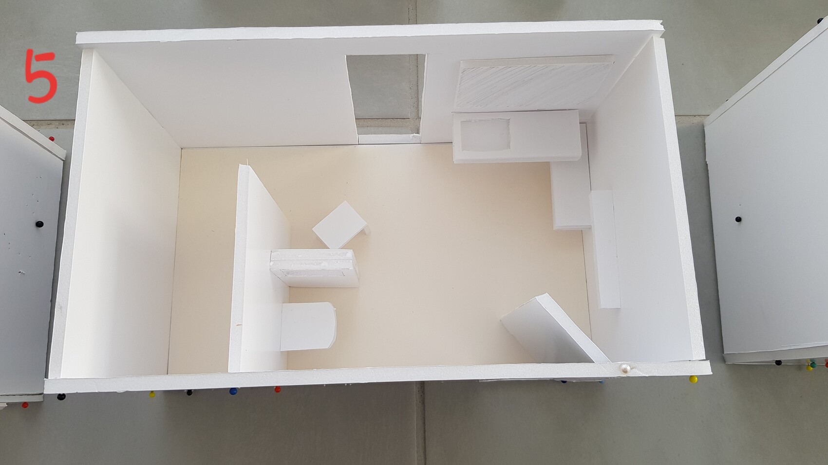 White interior diorama with partition walls, shelves, and square furniture on a beige floor.