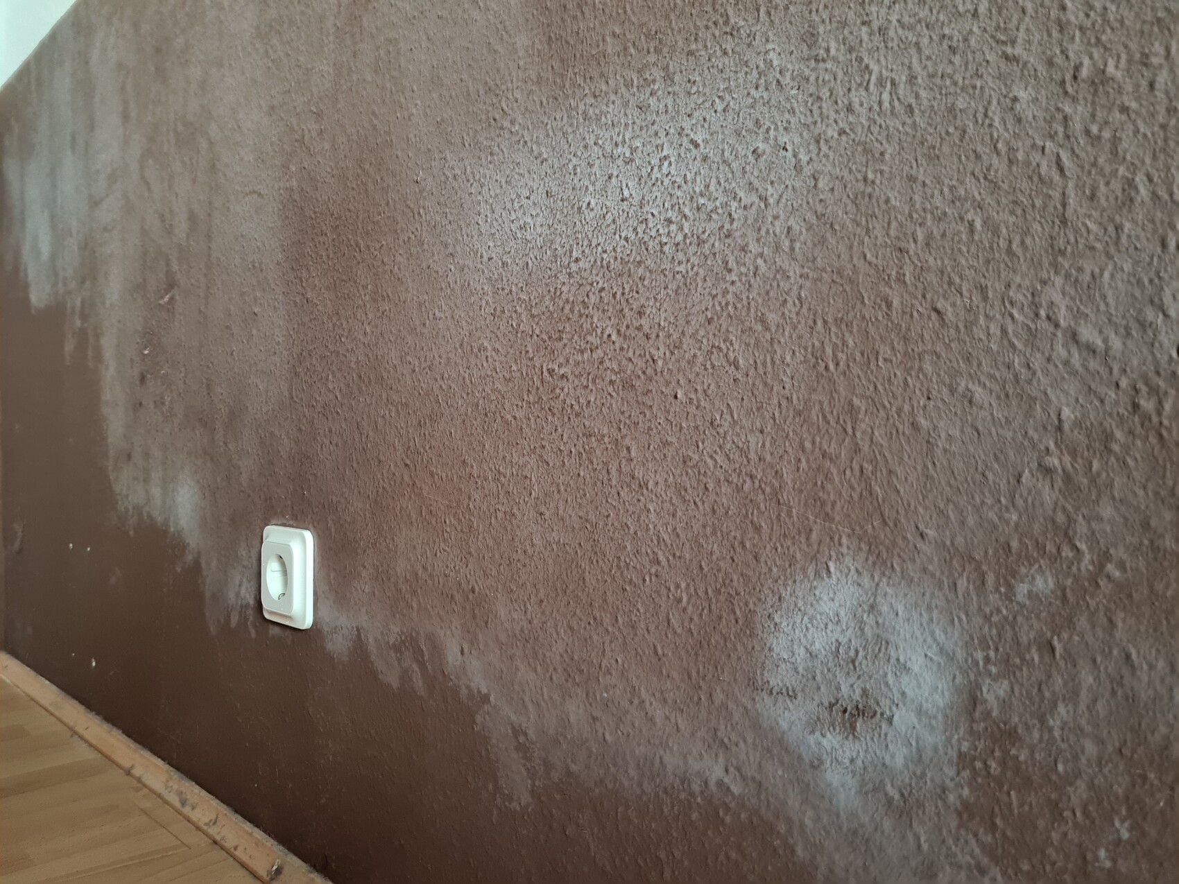 Rough brown wall with texture; white socket bottom left, wooden baseboard visible.