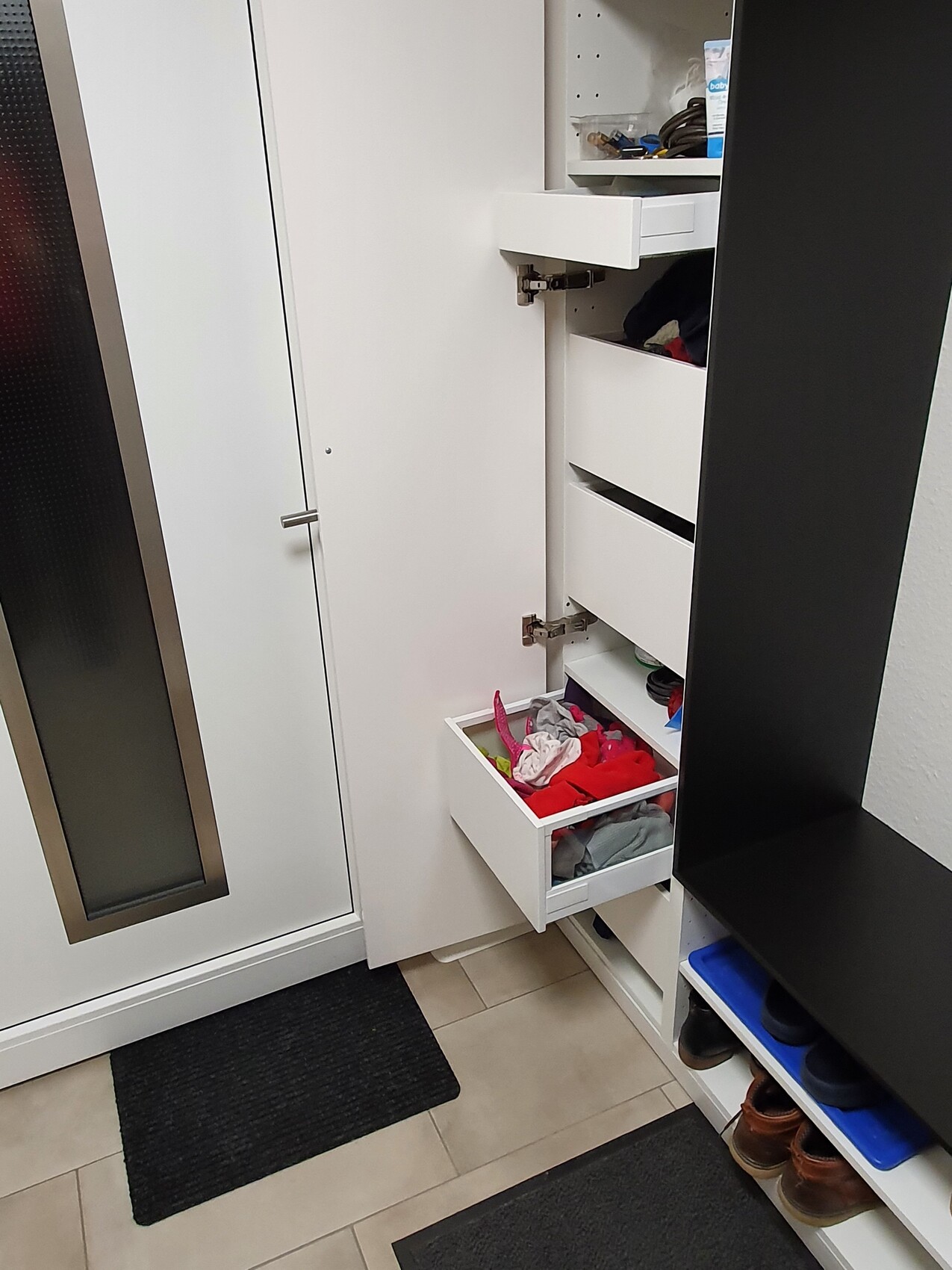 Weiße Garderobe mit offenen Schubladen, darunter Schuhregal mit Schuhen; Flur mit Fliesen.