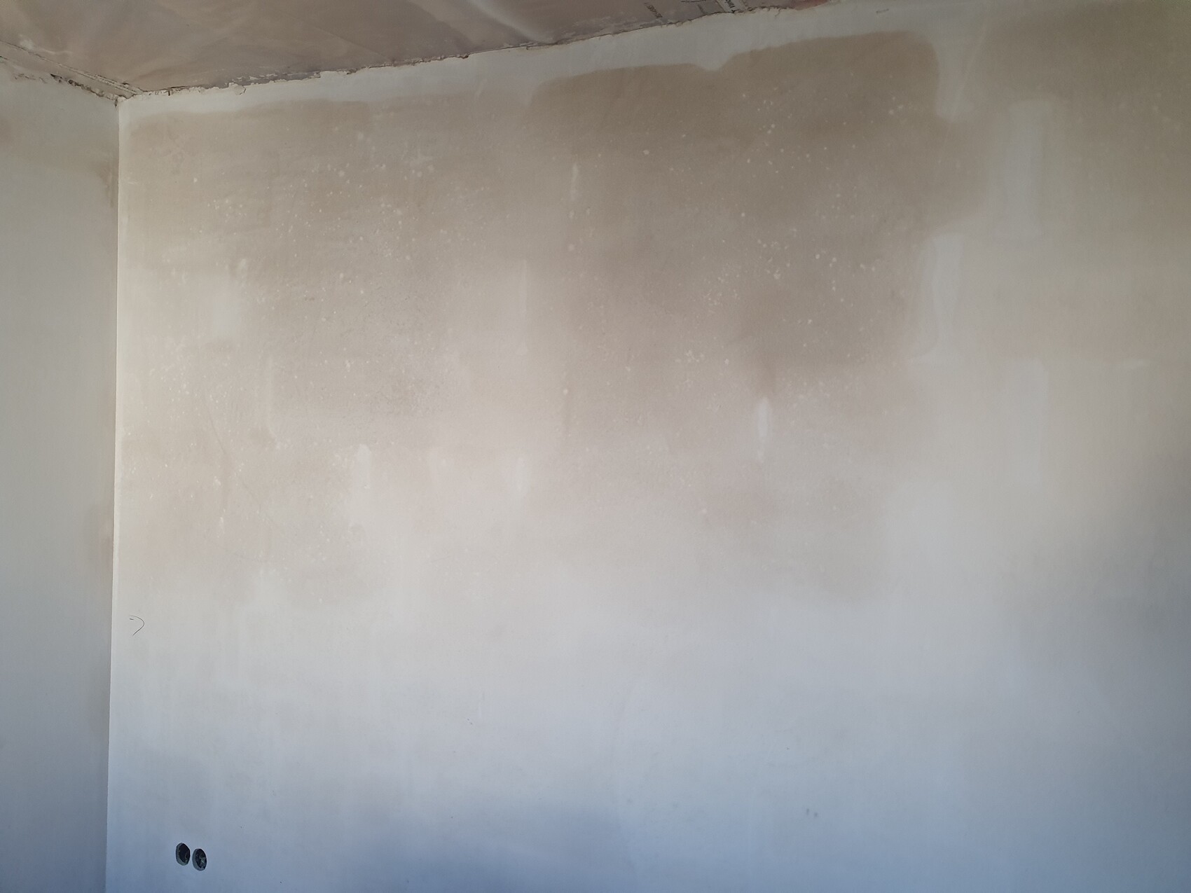 Unplastered interior wall with plaster patches, visible corner, two holes at bottom left.