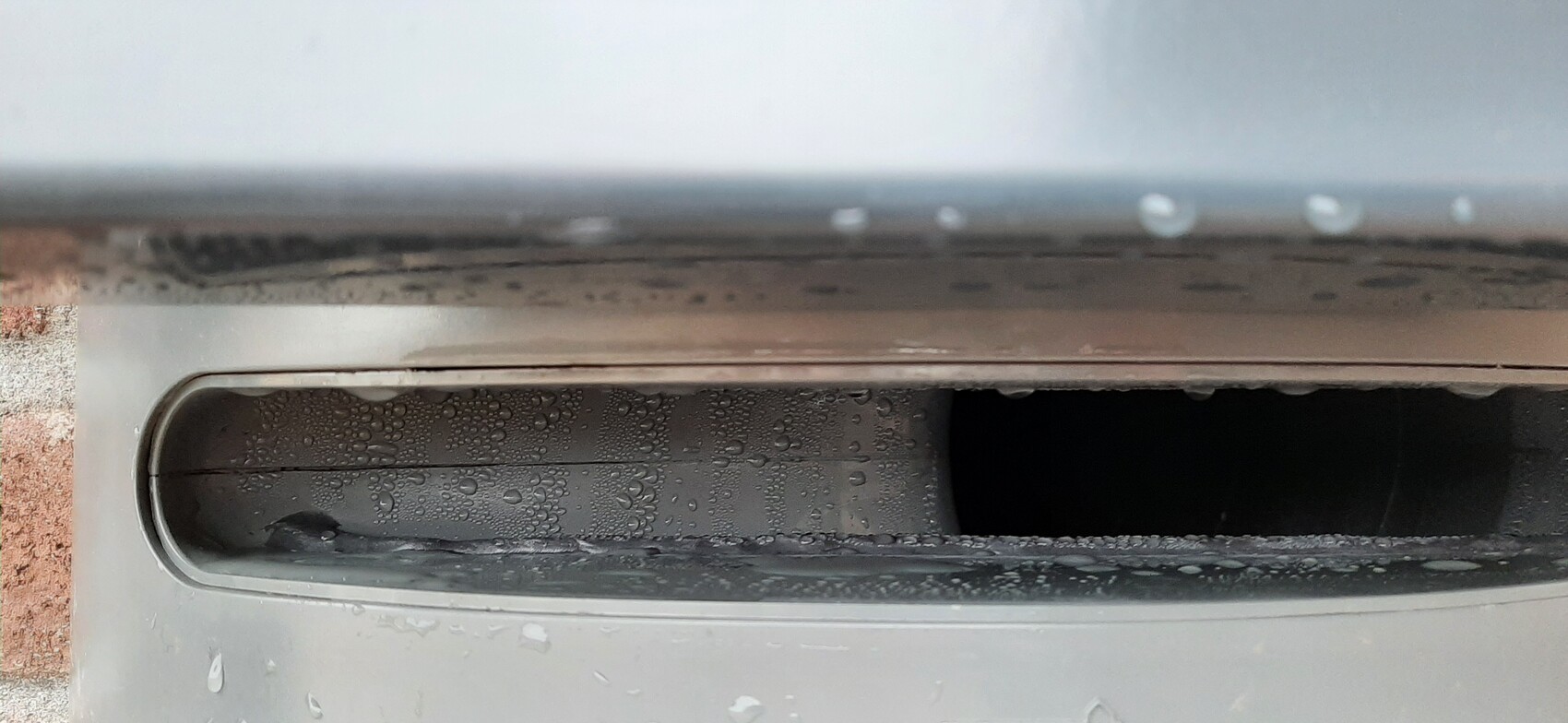 Close-up of a metal slot with water droplets and dark interior.