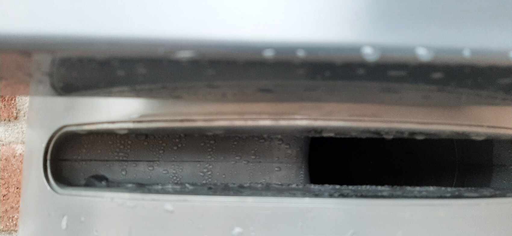 Close-up of a flat metal slot opening with water droplets inside, presumably a toaster.