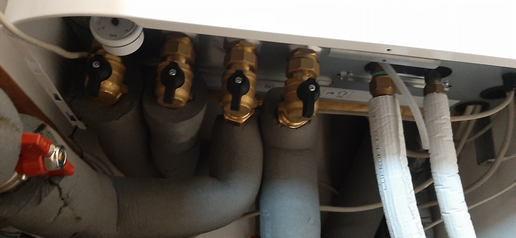 Under the heating unit: four brass valves with black handles and insulated pipes.