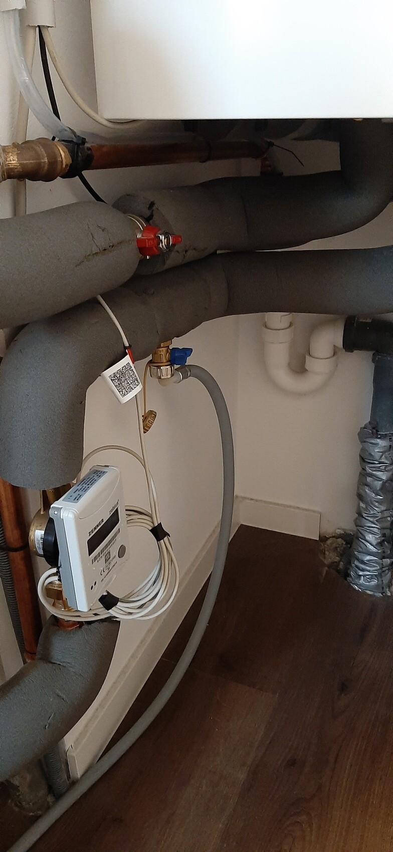 Under the boiler: insulated pipework, red shut-off valve, ZENNER water meter with cable harness.