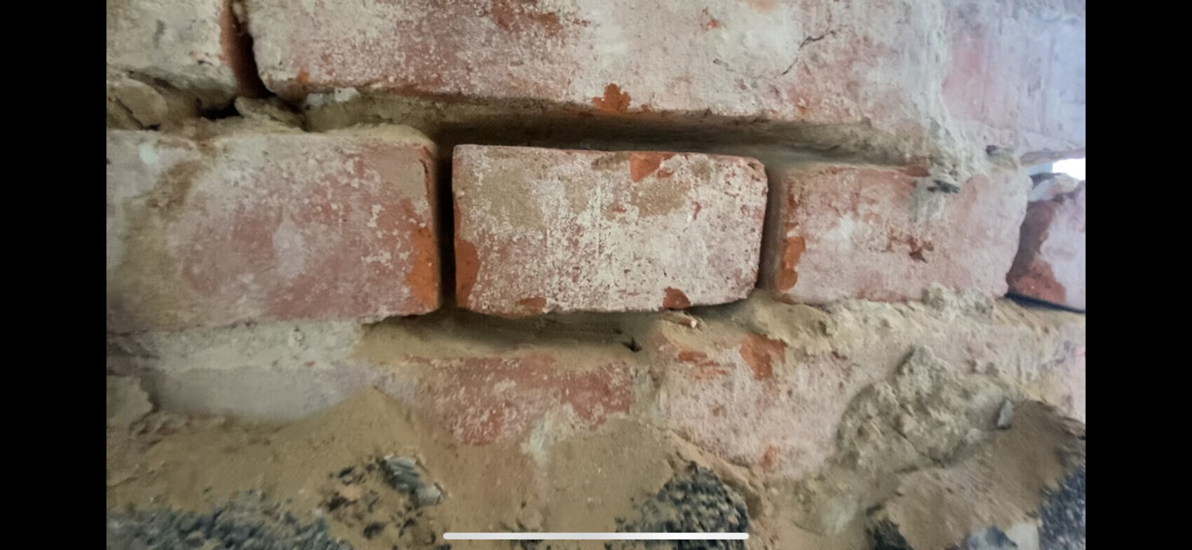 Brick wall made of red bricks with visible mortar joints; dust and soil on the floor.