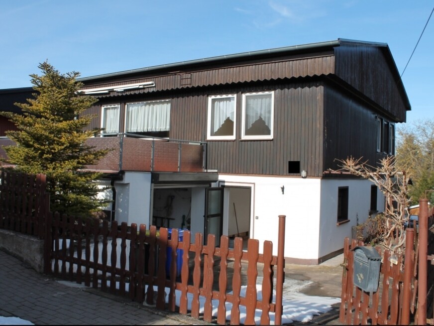 Two-story house with dark wood facade and white base, open garage area, wooden fence.