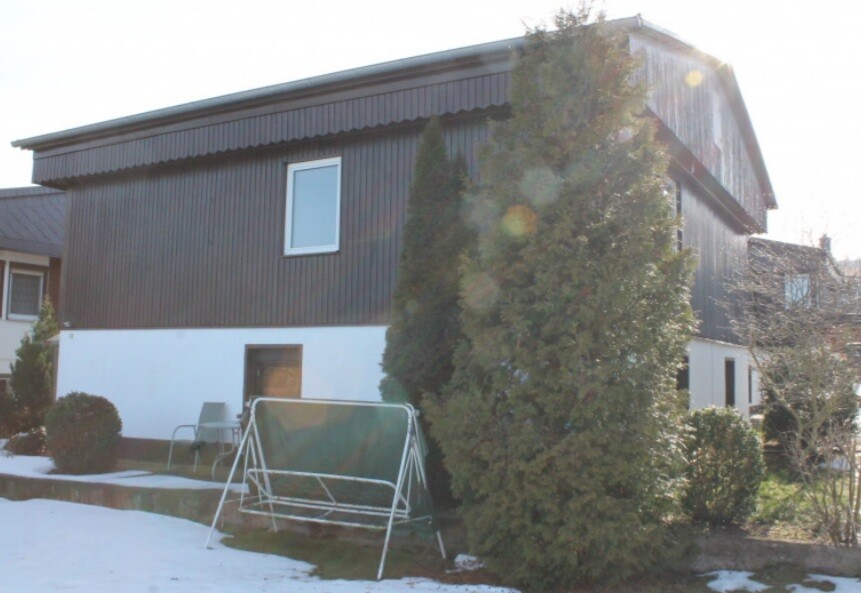 Two-story house with dark wood facade, white base, snow and a metal gate in front.