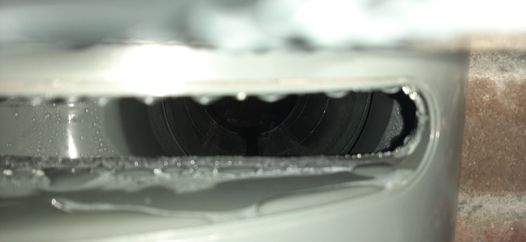 Close-up of a black inner pipe in a light gray metal housing with droplets