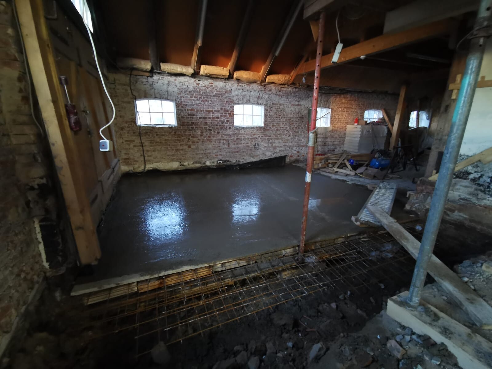 Basemented construction site with damp concrete floor, brick walls, metal supports and building materials.