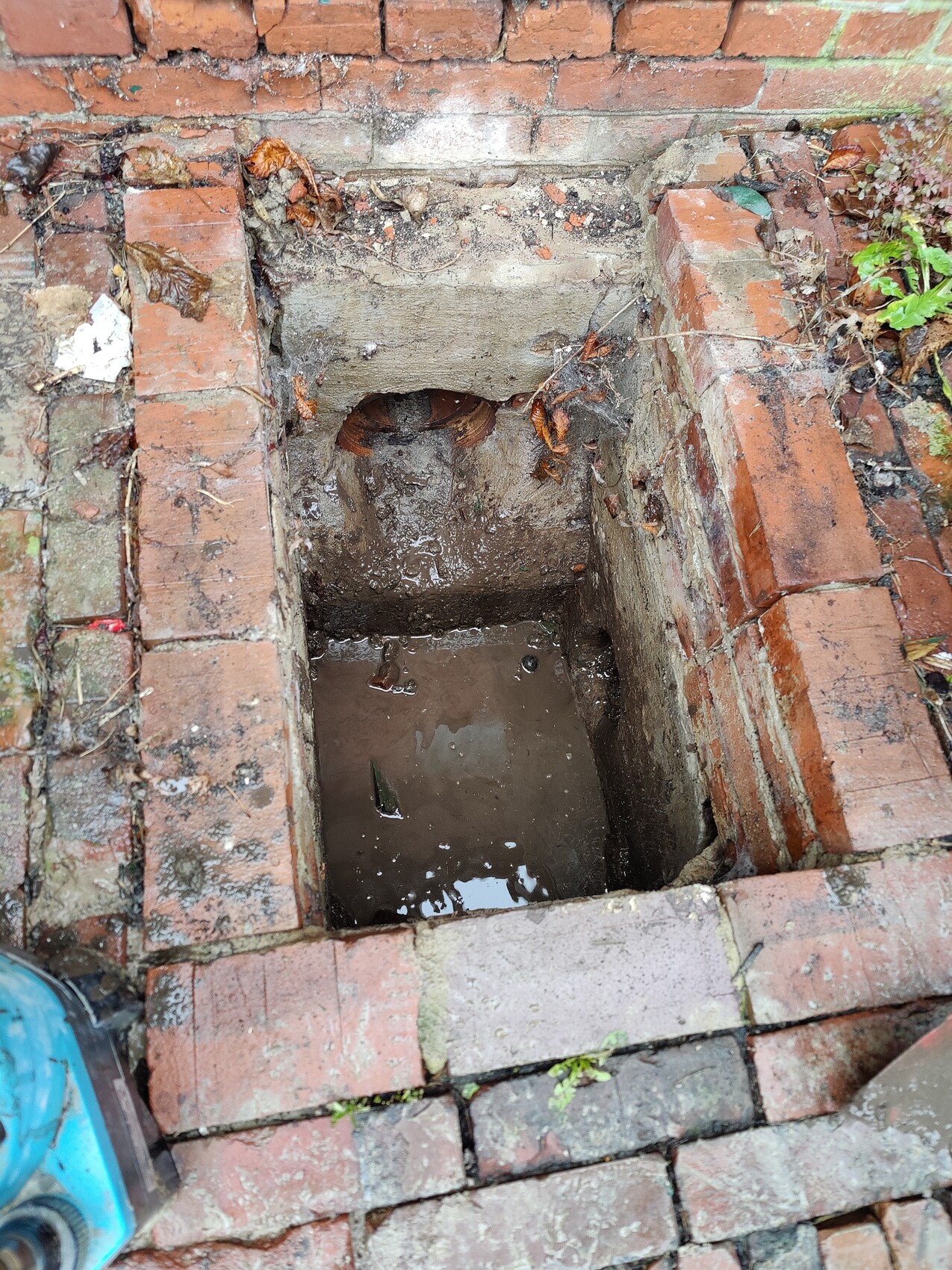 Open brick shaft with standing water in a paved environment.