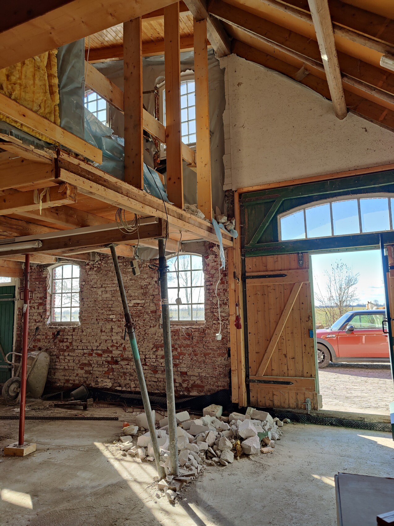 Construction site interior: exposed brickwork, wooden beams, debris, open gate with car outside.