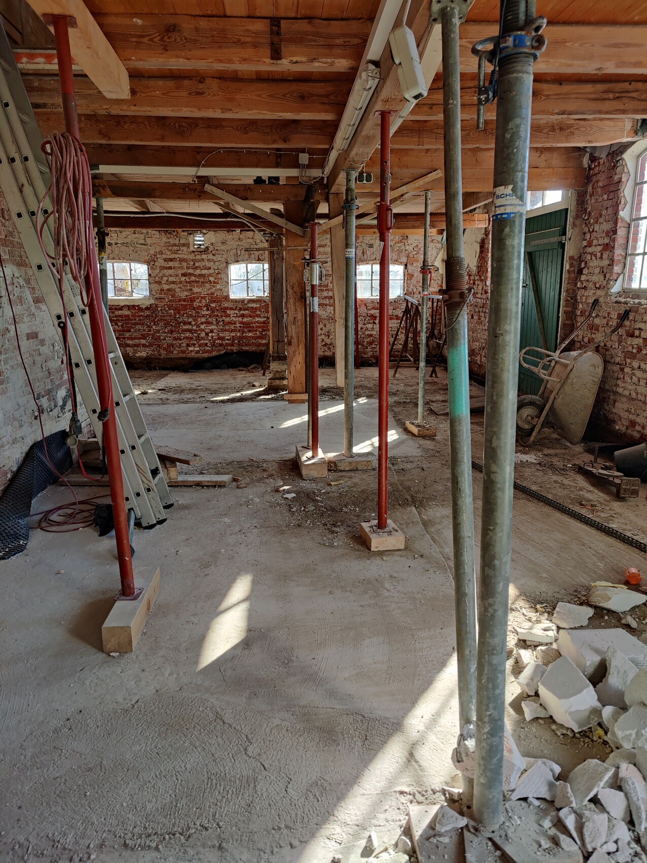 Construction room with red support props, wooden beam ceiling, rubble stone walls, debris and tools.