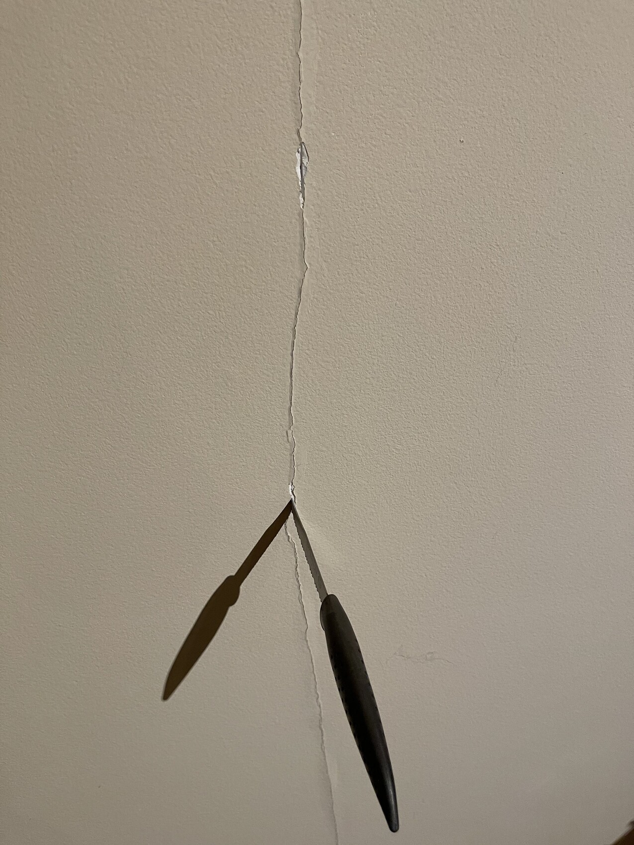 Beige wall/ceiling with vertical crack; two blades of a tool inserted into the gap.