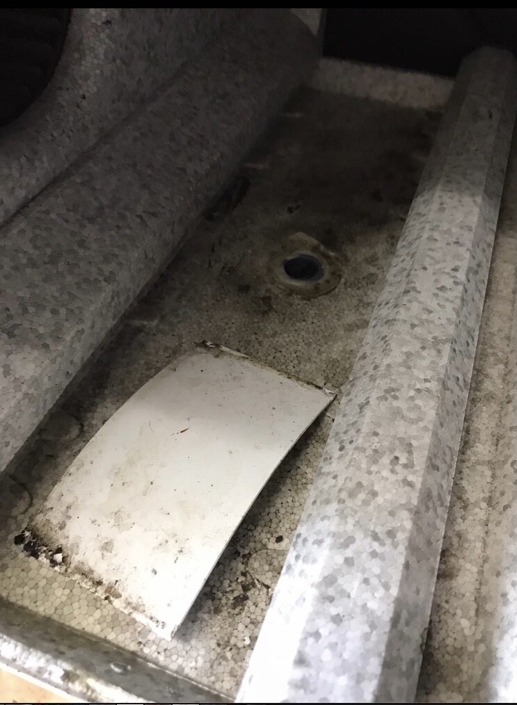 Interior view of a dusty metal tray with a loose white metal part and deposits.