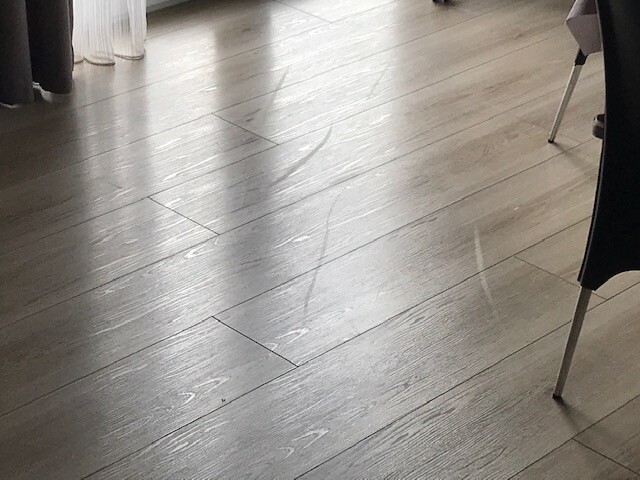 Holzboden mit langen Kratzspuren, Spuren auf hellgrauem Holz, Ecke eines Stuhls sichtbar.