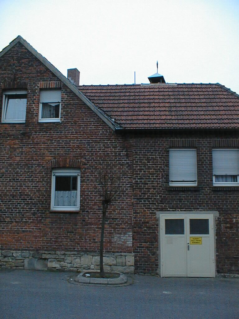 Brick house with red tiled gable roof, small tree in front yard, white doors and windows