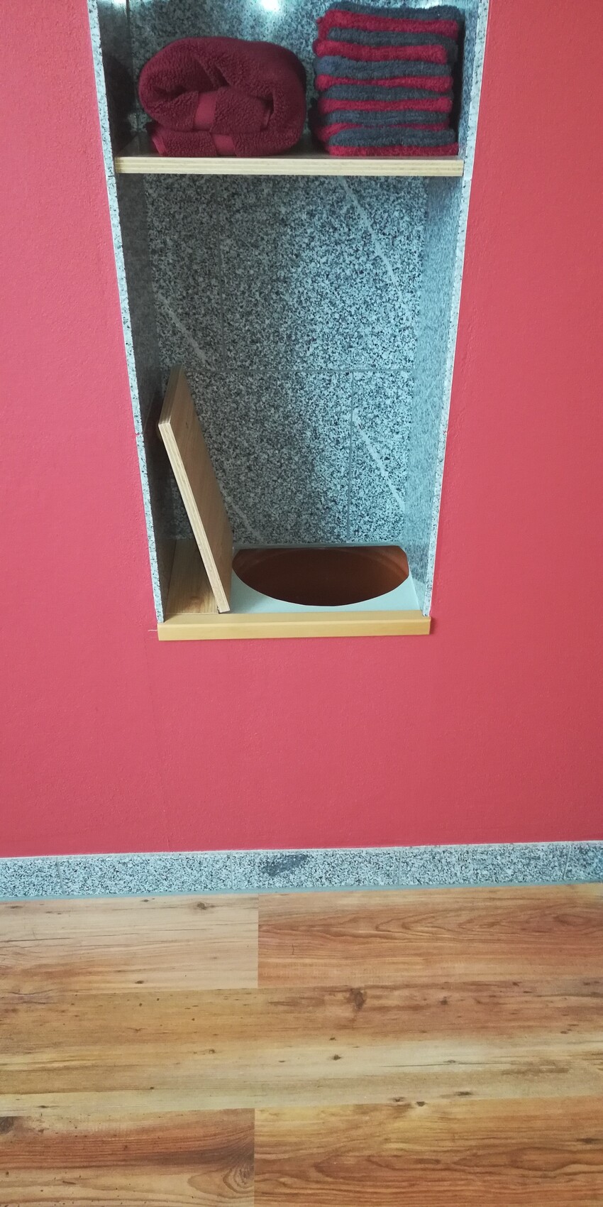 Red bathroom wall with open niche made of granite, stacked towels on the shelf