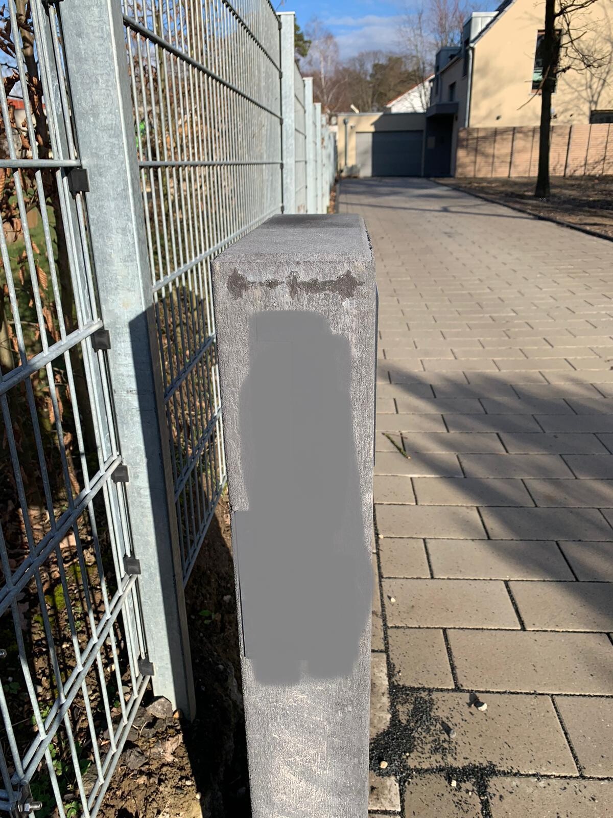 Walkway with gray concrete post next to metal fence; large gray stain on the post.