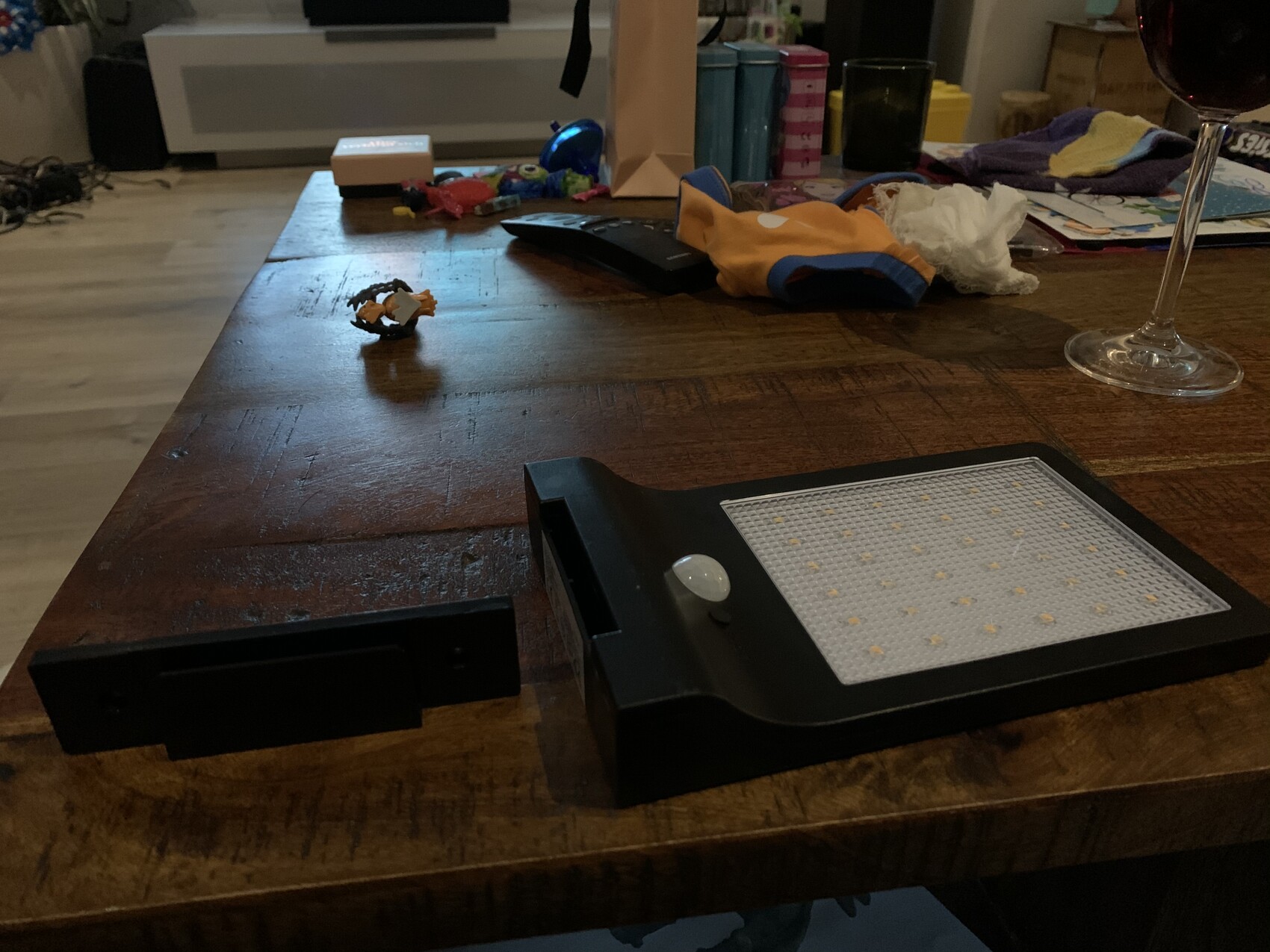 An LED light panel lying on a wooden table; wine glass on the right, small parts scattered on the left.