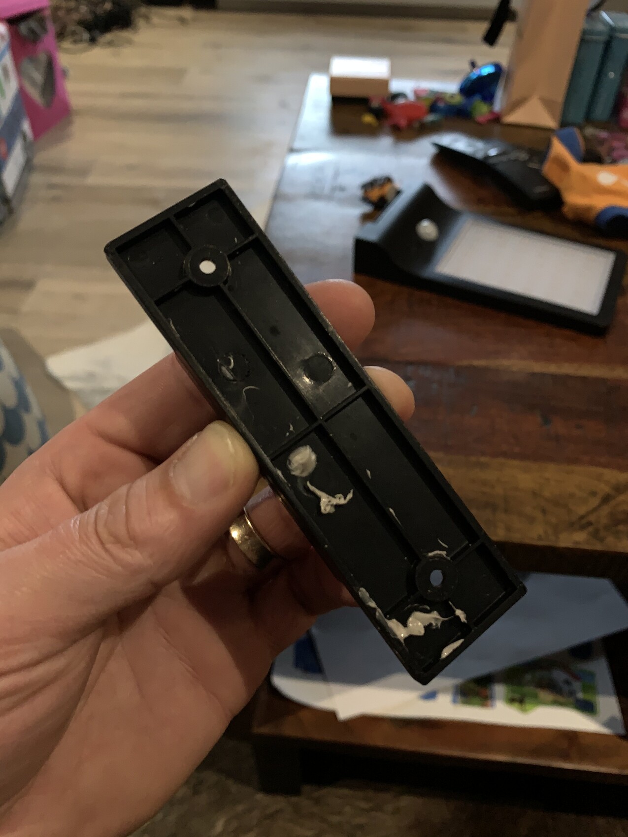 Close-up: hand holding black plastic piece with two round indentations; table in the background.