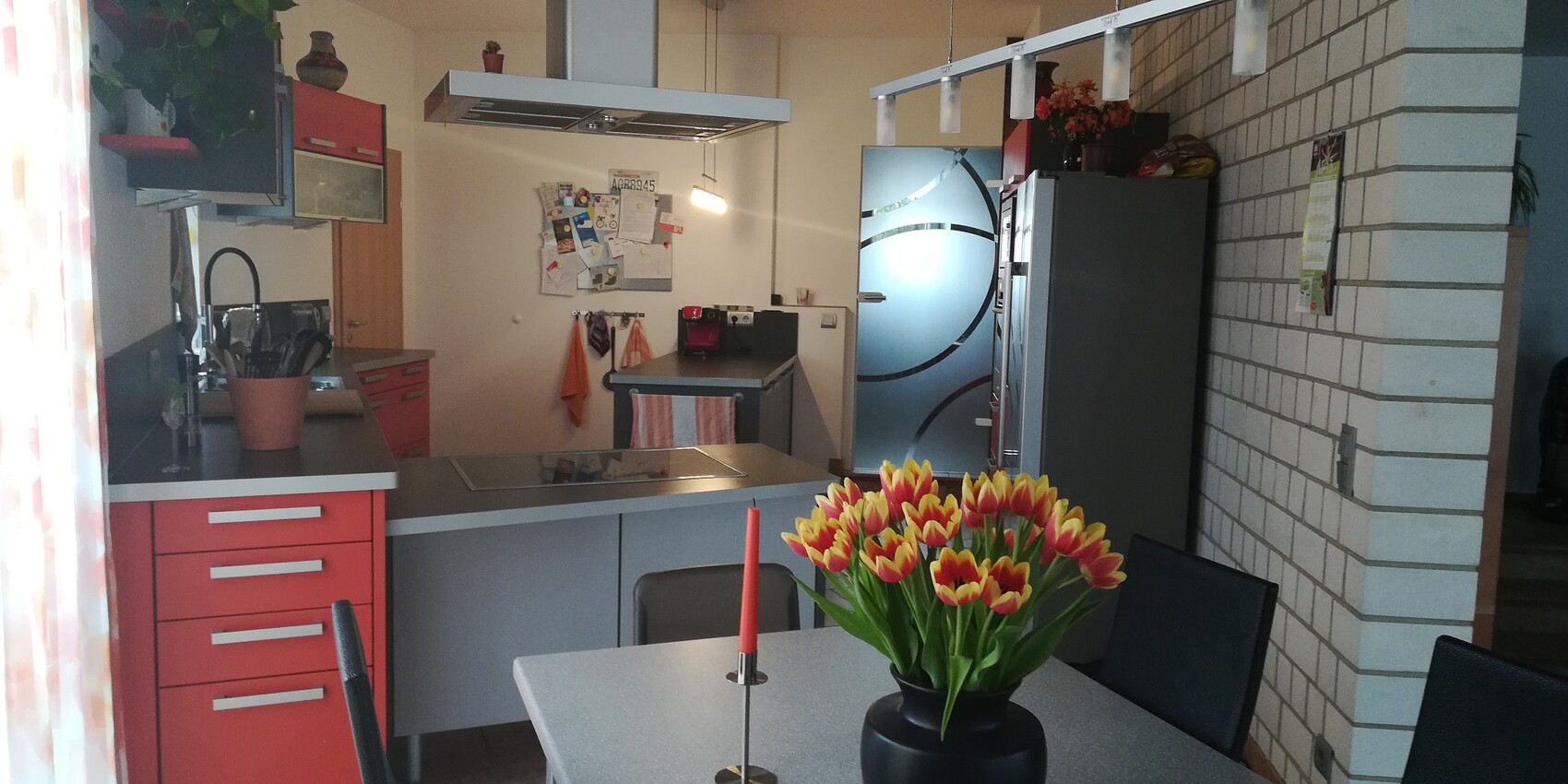 Modern kitchen with red drawers, kitchen island, dining table, and tulips in the foreground.