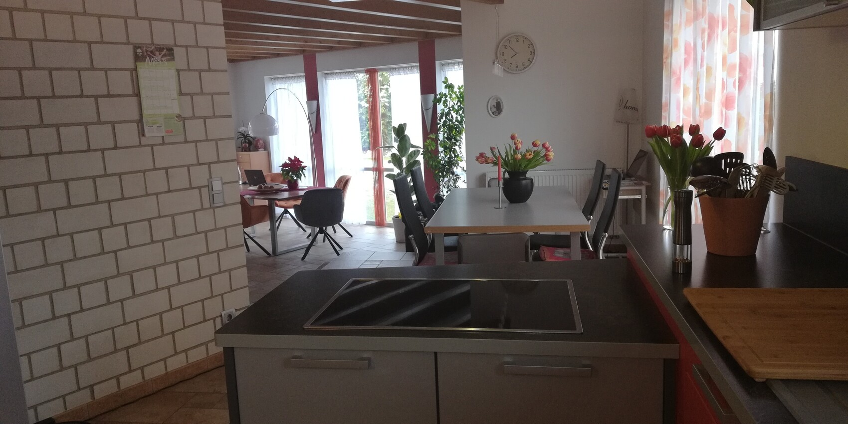 Open kitchen with cooking island, dining table, tulips, and houseplants on the windowsill.