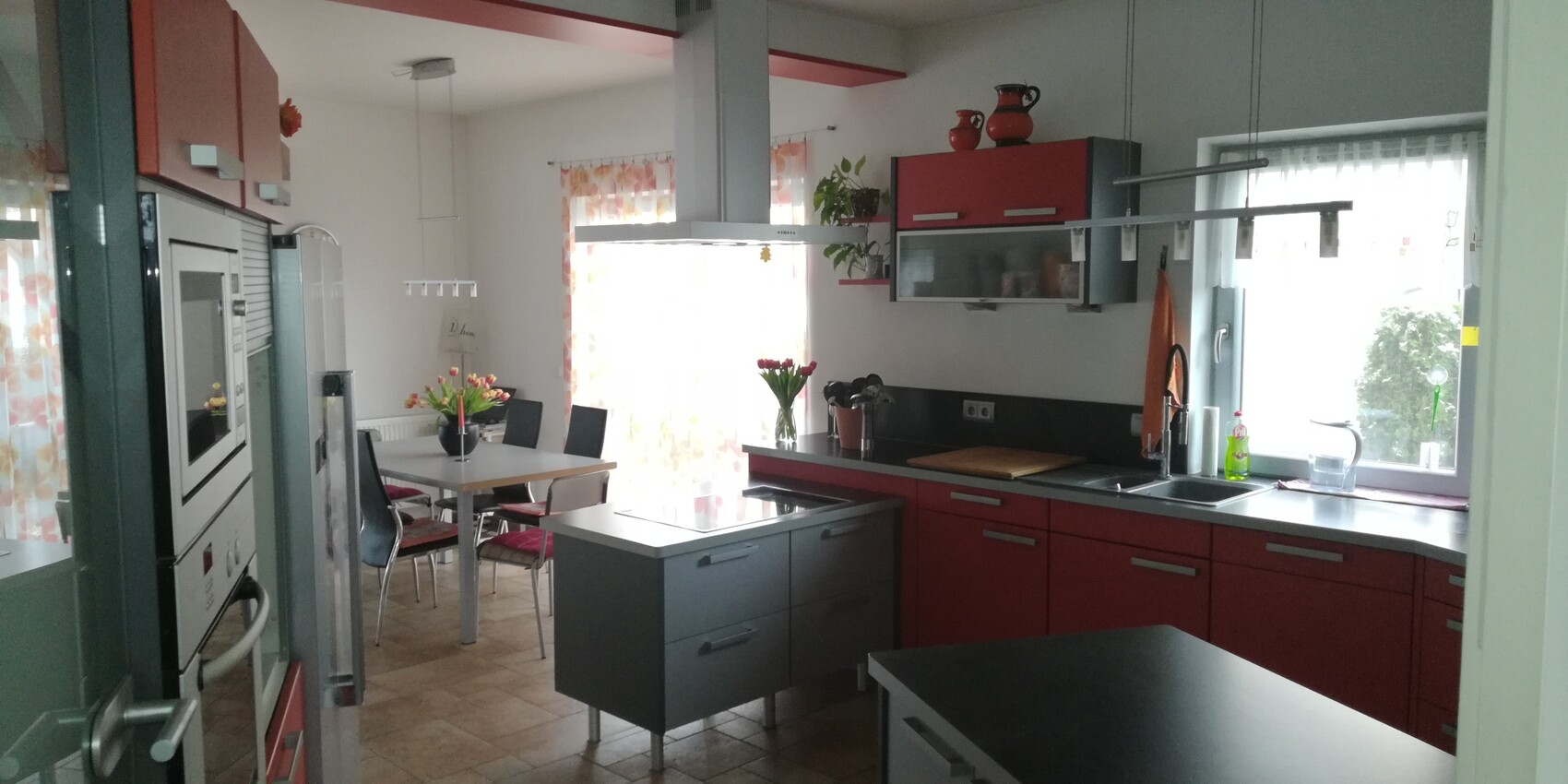 Modern kitchen with red cabinets, cooking island, dining table, and tulips.