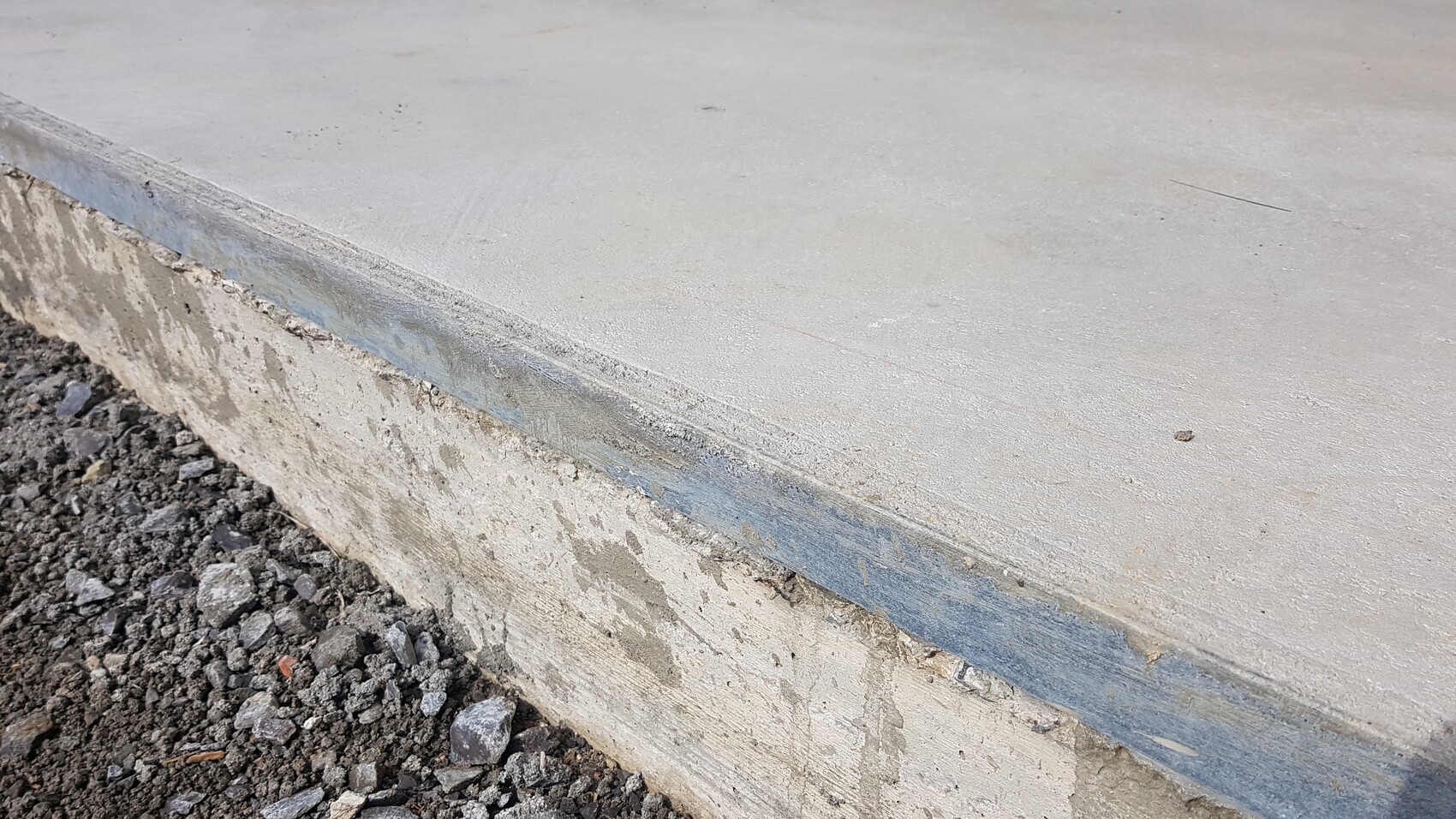 Concrete slab with edge, blue border strip, and loose gravel on the floor.