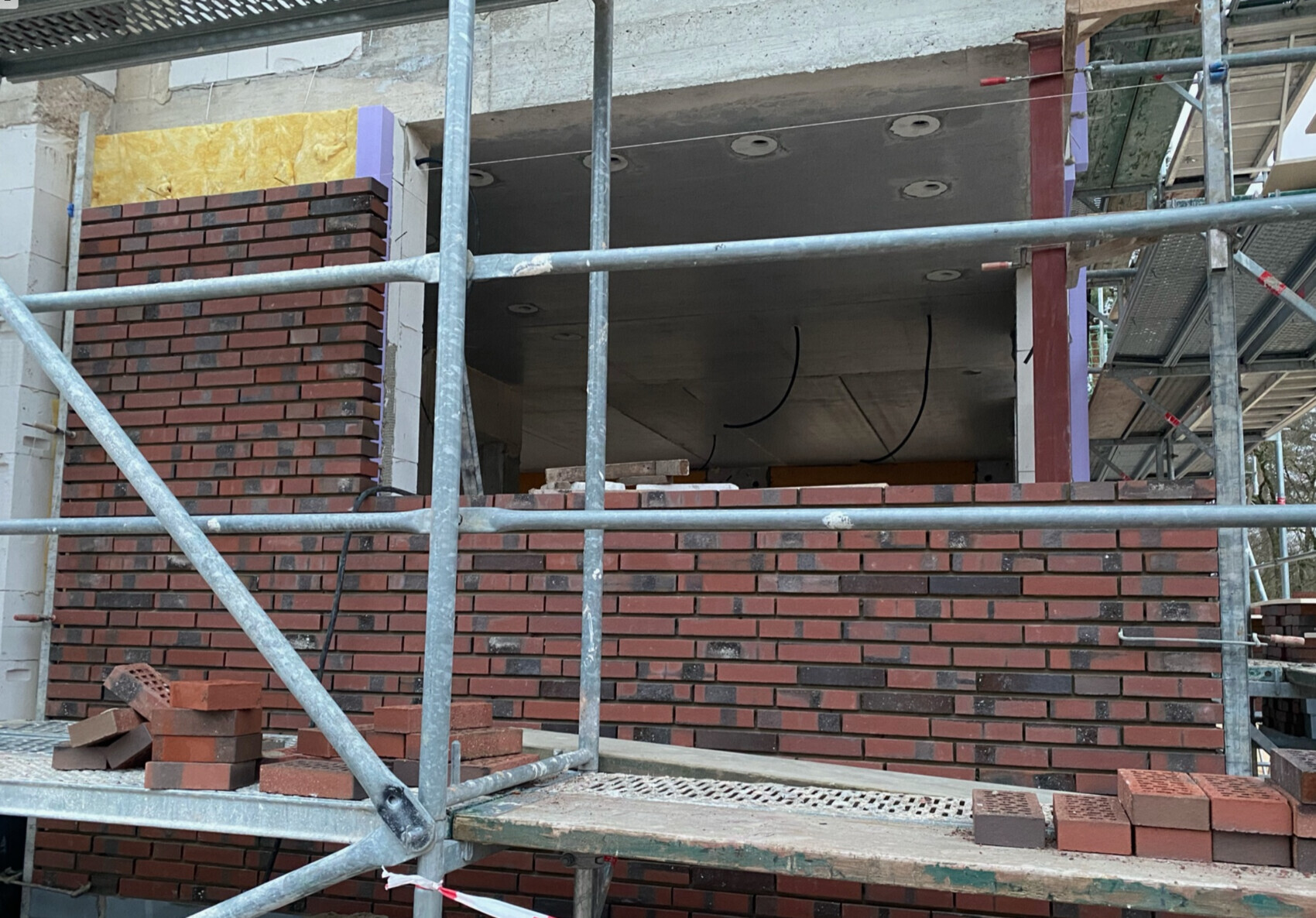 Scaffolding in front of red brick wall, construction work on facade, visible opening in building