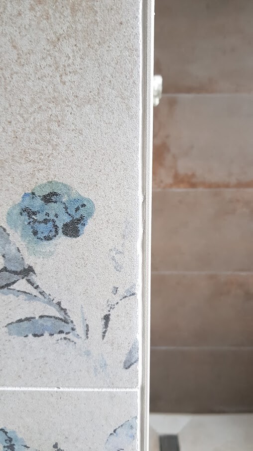 Wall tile with blue floral motif on cream background, side edge visible.