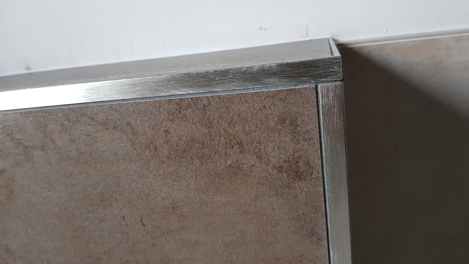 Close-up of a metal frame with brown panel on a piece of furniture edge.