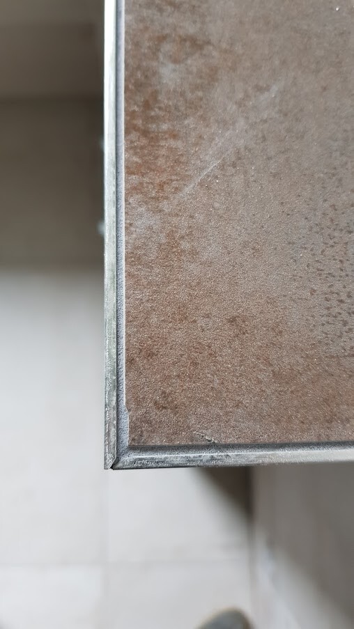 Close-up of a rusty metal plate with silver frame on the lower left corner.