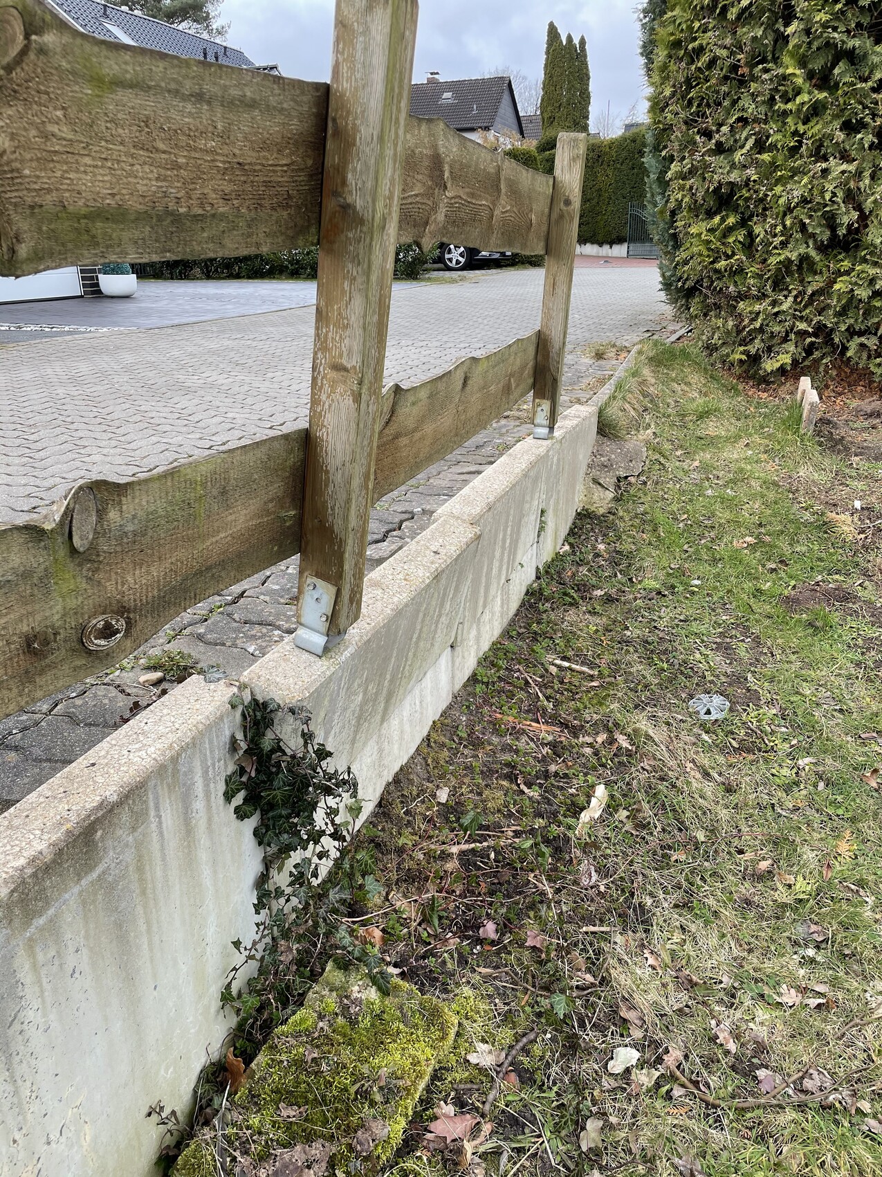 Weathered wooden railings on a concrete wall next to a paved driveway.
