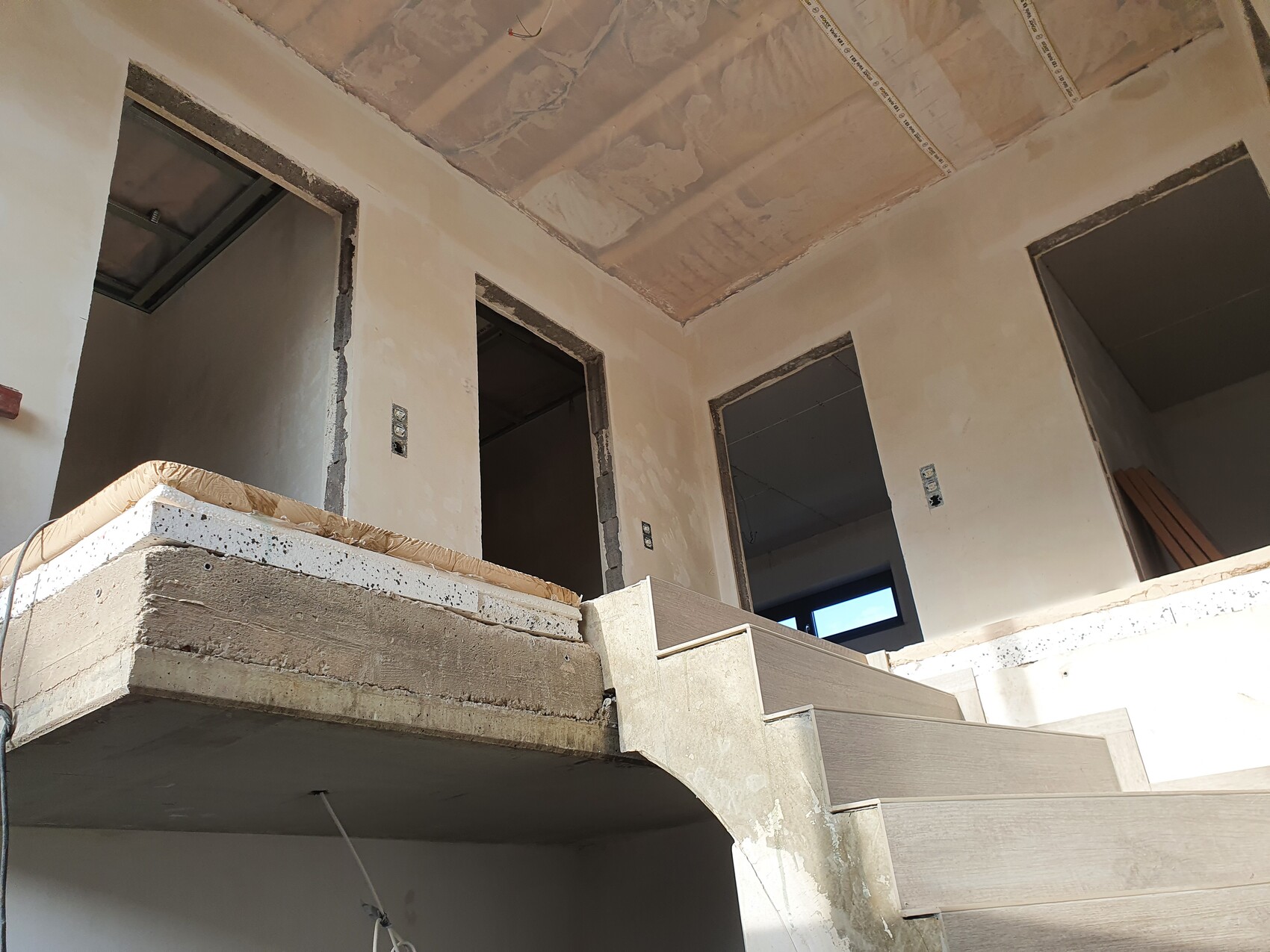 Unfinished interior of a building: wooden staircase, open door frames, and rough walls.