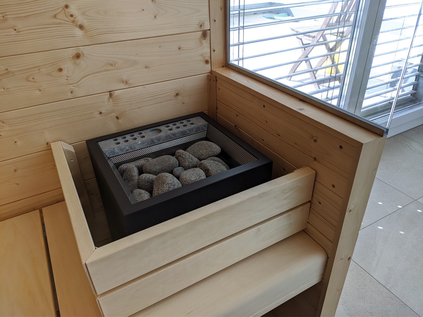 Sauna stove with visible stones in a wooden sauna, surrounded by benches