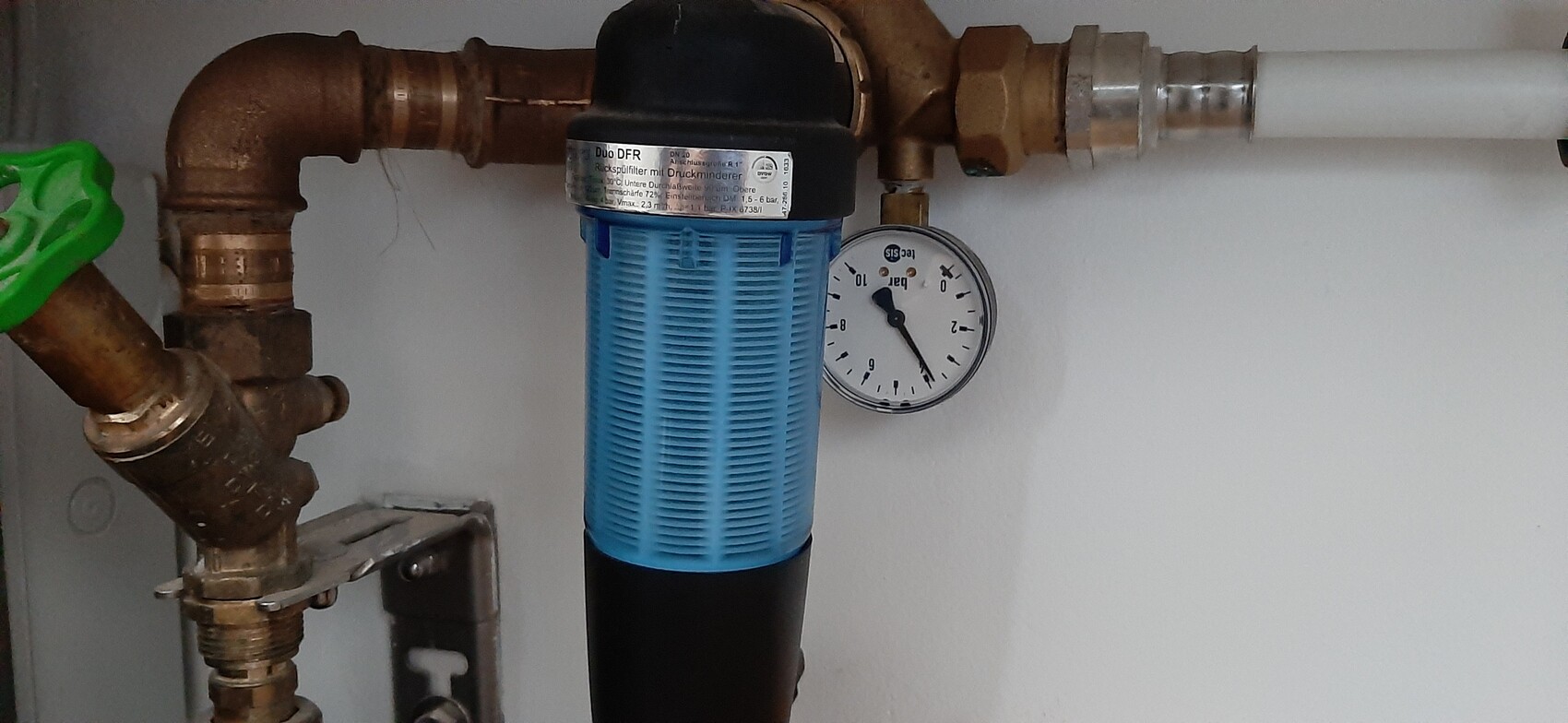 Rusted copper pipes with green valve, blue filter housing, and pressure gauge.