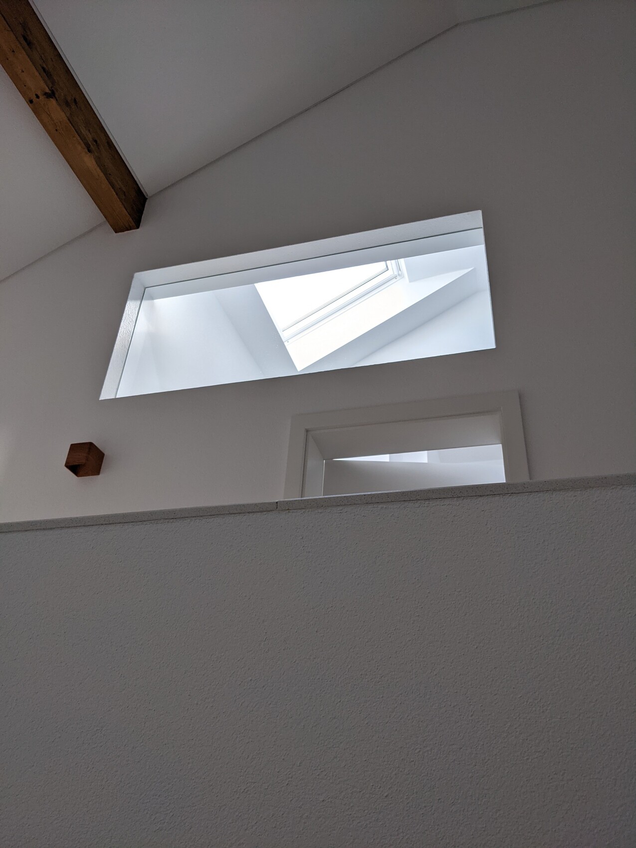 Bright interior with sloped roof window, white walls, and wooden beams.