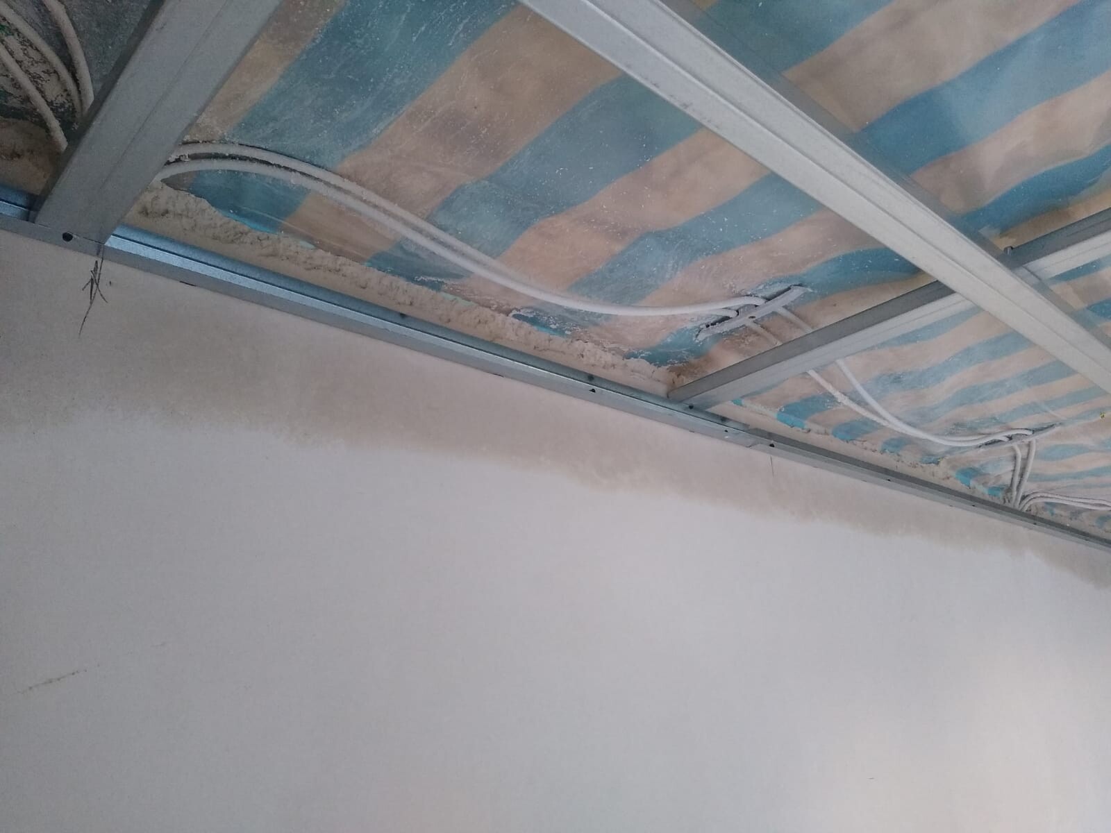 Construction scene: metal stud frame, loose insulation, visible cables on the ceiling.