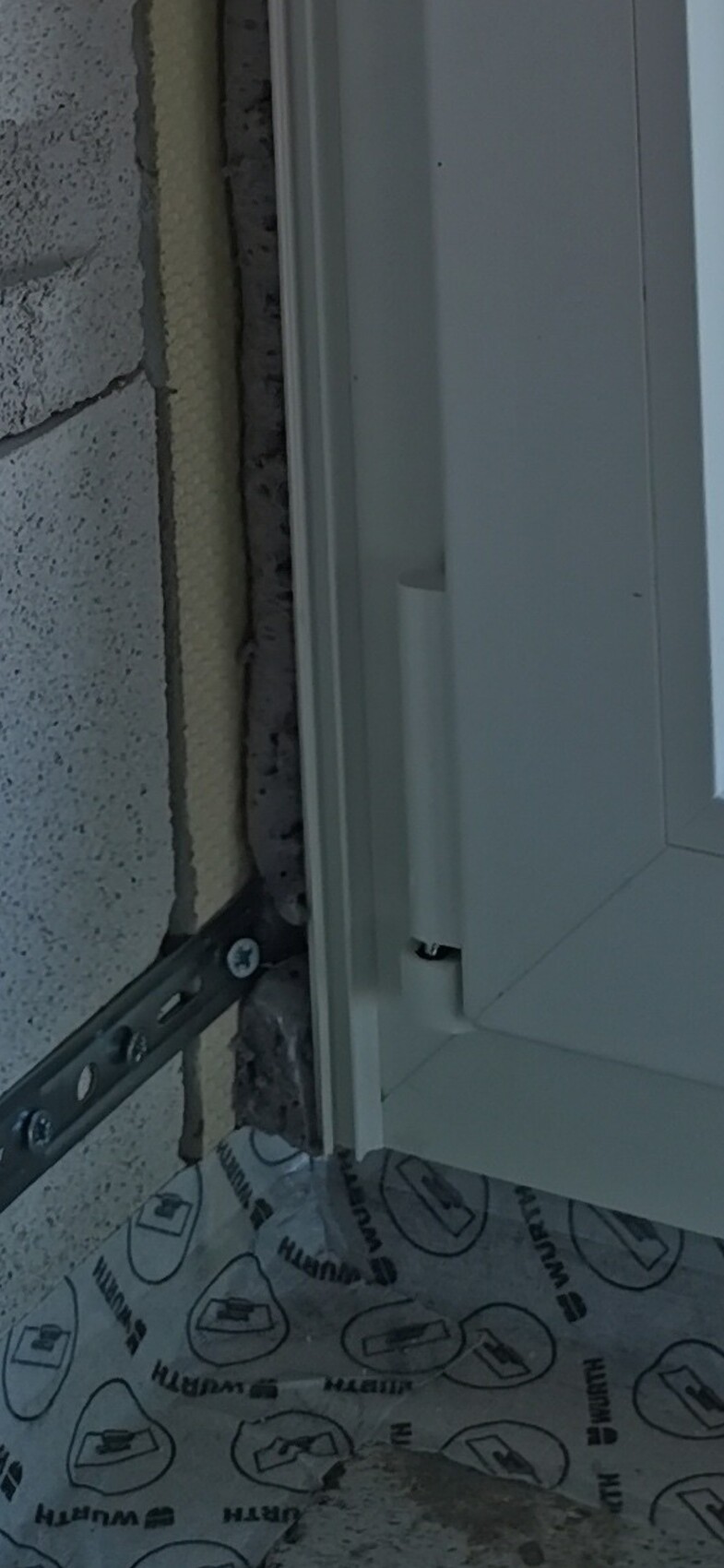 Close-up of a white window frame on a concrete wall with insulation and mounting rail.