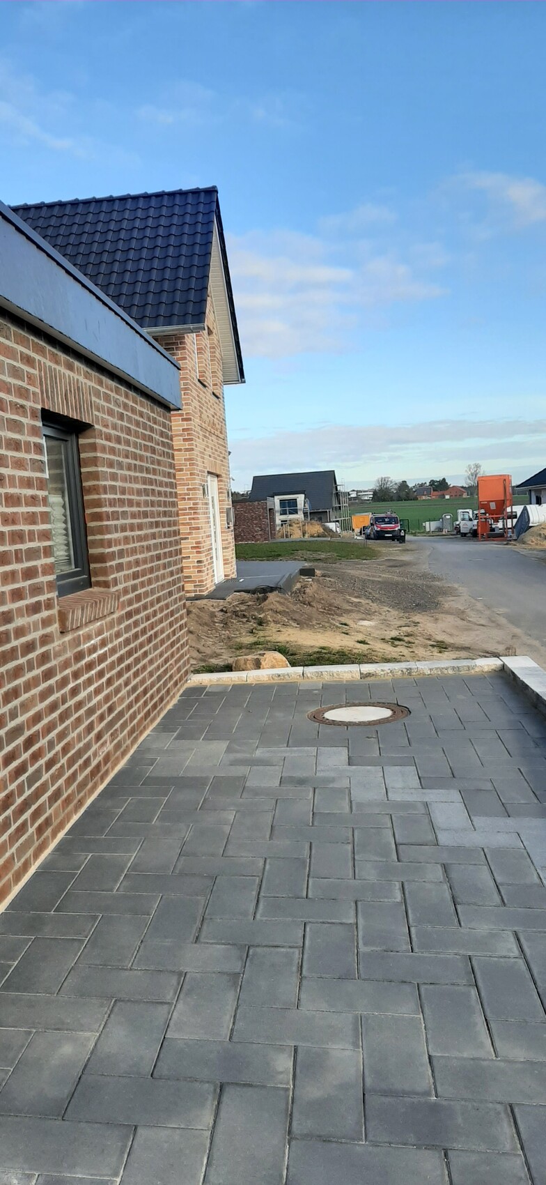 New development with brick houses and paved forecourt; construction equipment in the background.