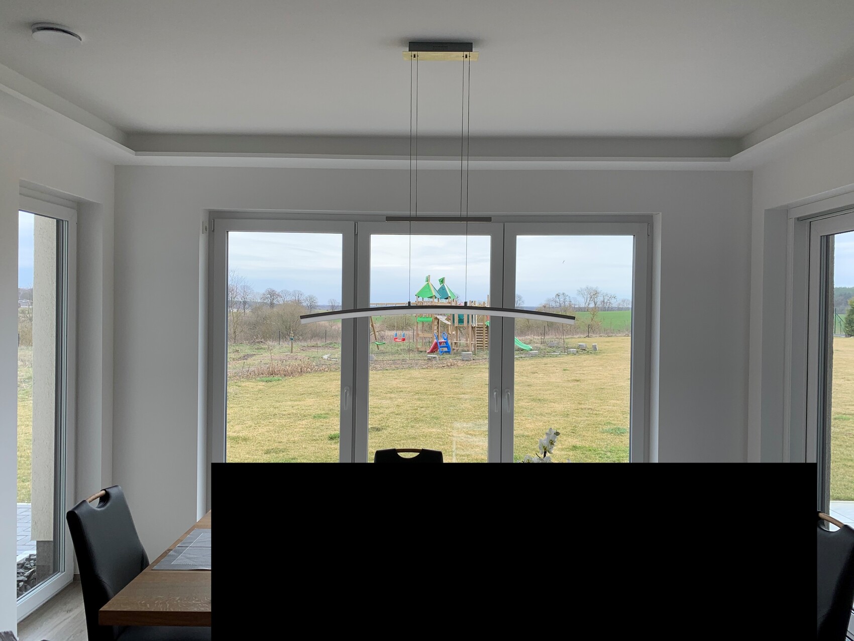 Bright living space with dining table, black chairs, and large window with garden view.
