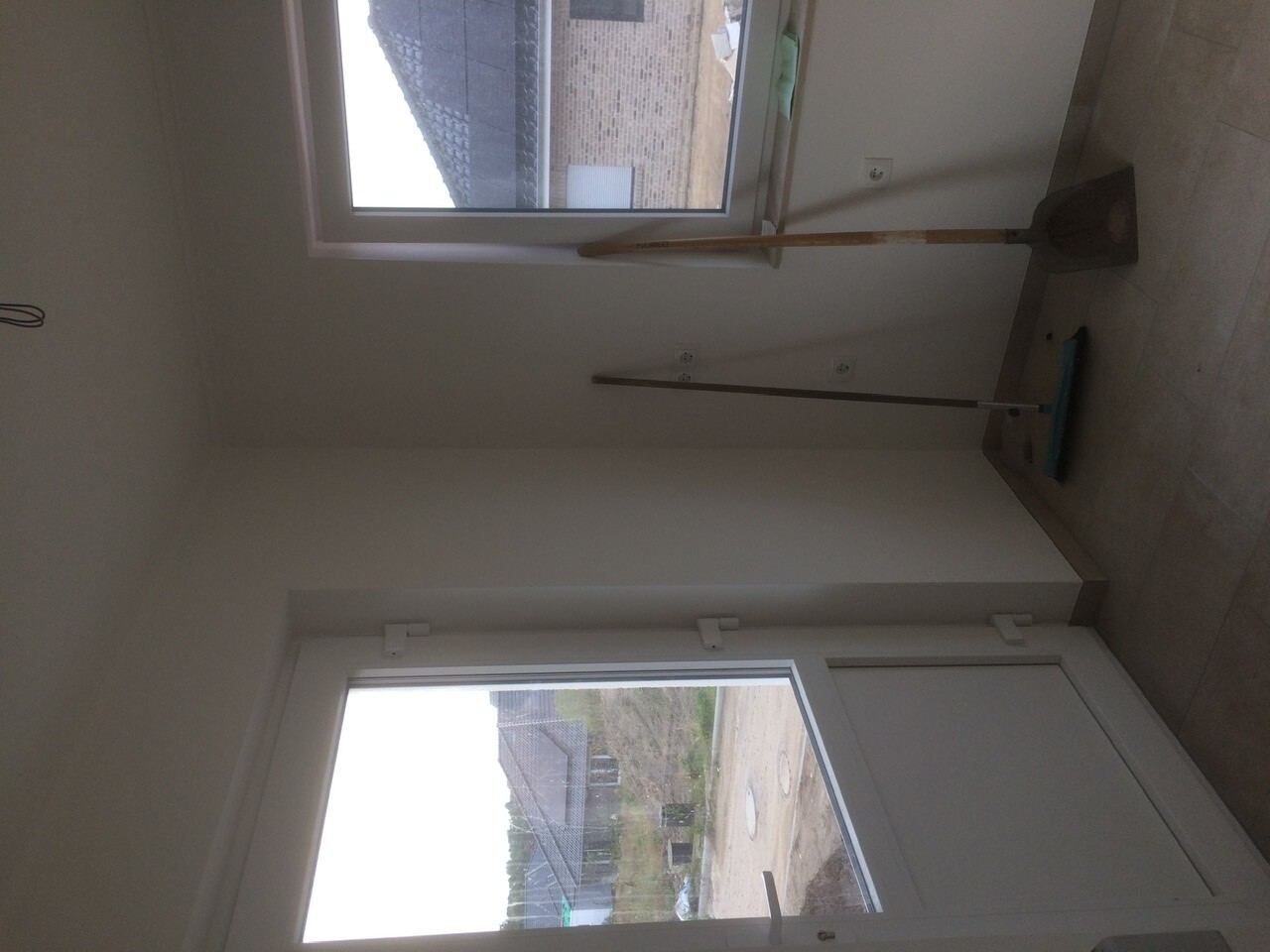Leerer Innenraum mit Fensterfront; Besen, Kehrblech und Mopp lehnen an der Wand.