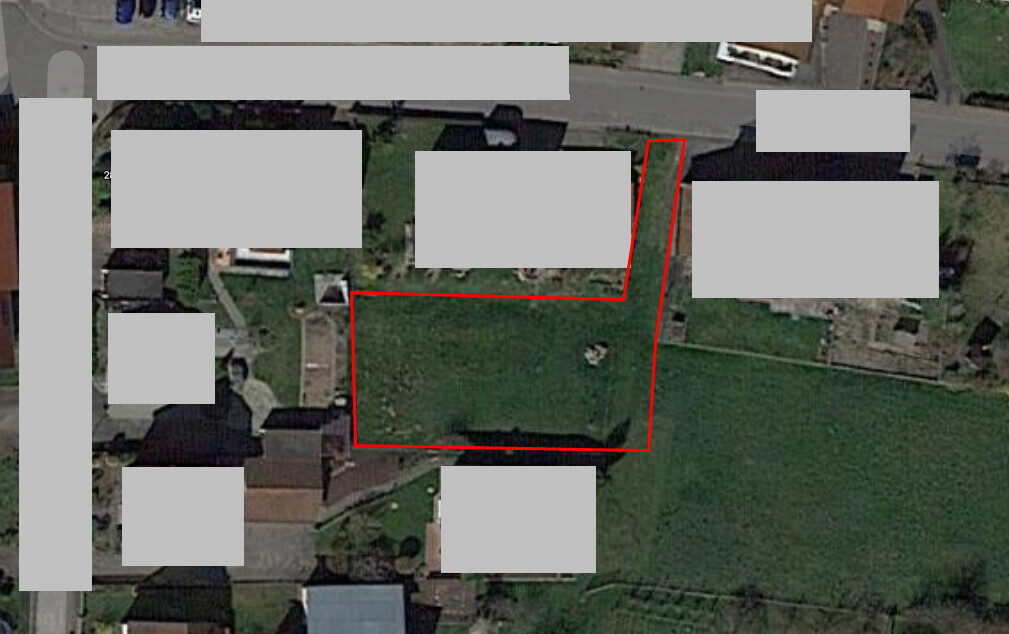 Aerial photo of a plot outlined in red on a green area between residential houses.