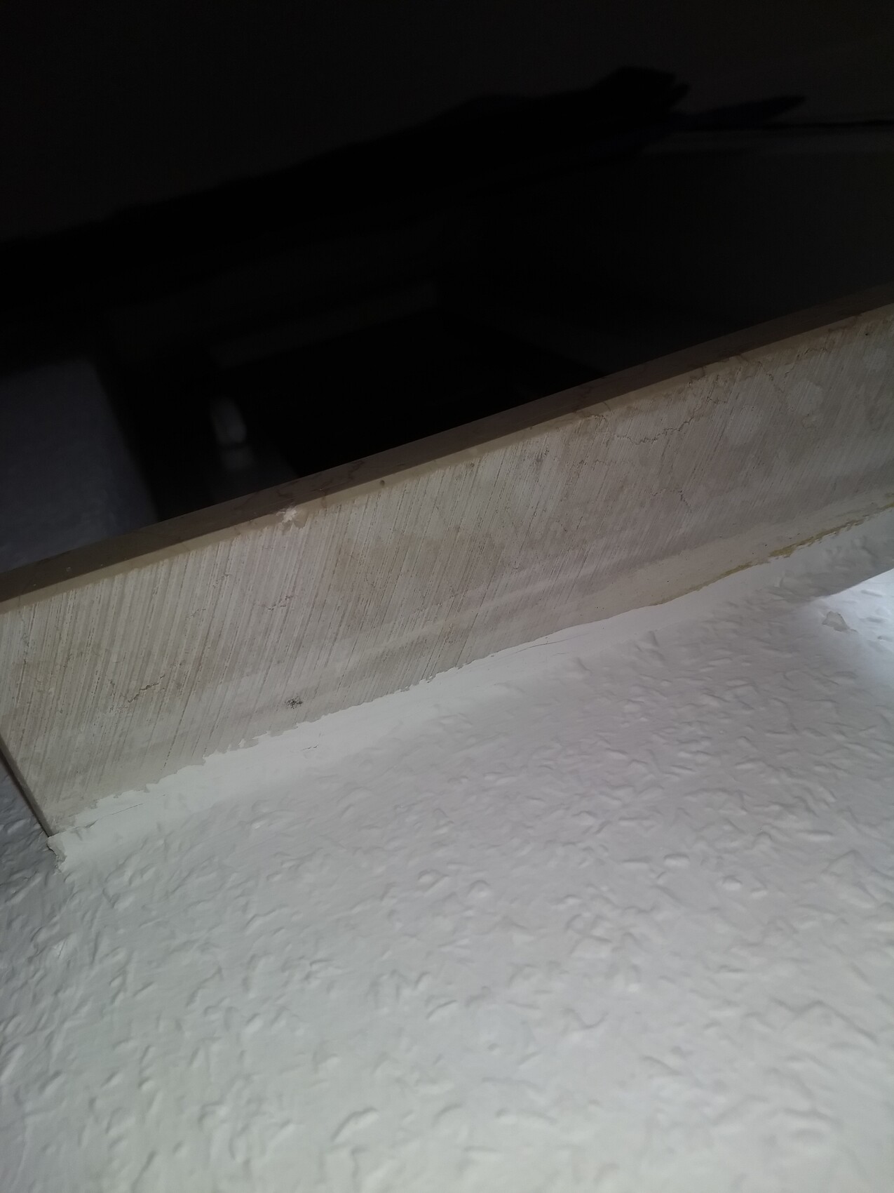 Dark space behind a wooden panel; in front, a white textured wall.