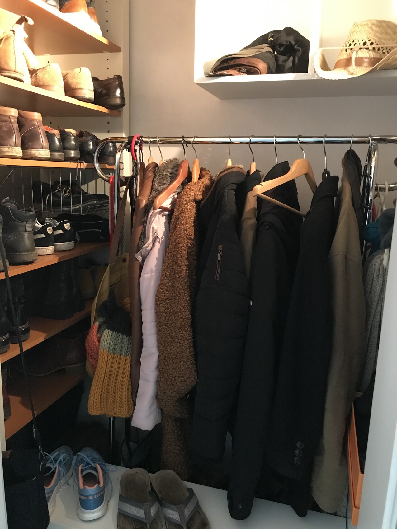 Open wardrobe with coats and jackets on a hanging rod, shoes on shelves.